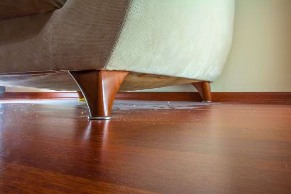 Poussi&egrave;re accumul&eacute;e sous un canap&eacute; pos&eacute; sur parquet.