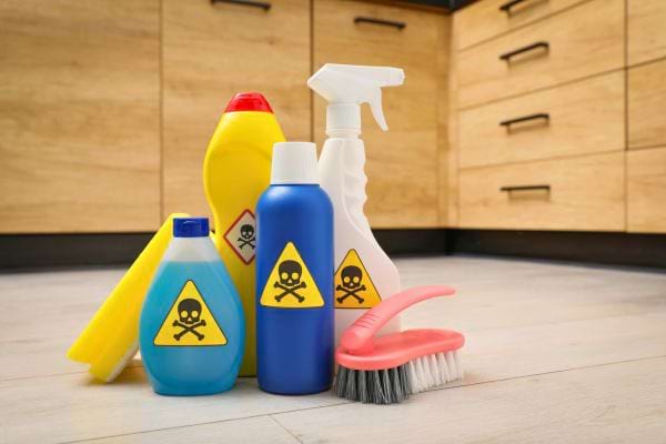 Plusieurs bouteilles de produits ménagers toxiques avec symboles de danger posées au sol.