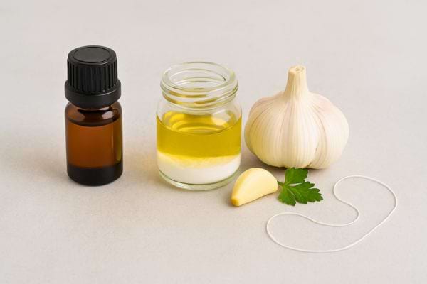 Flacon d’huile, gousse d’ail et persil posés sur une table.