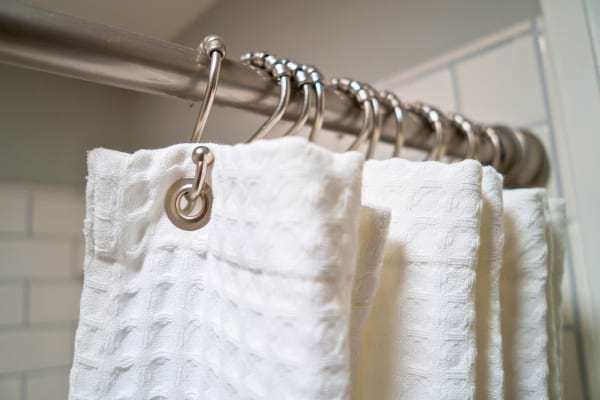 Un rideau de douche blanc est suspendu à une tringle métallique avec des anneaux en acier.