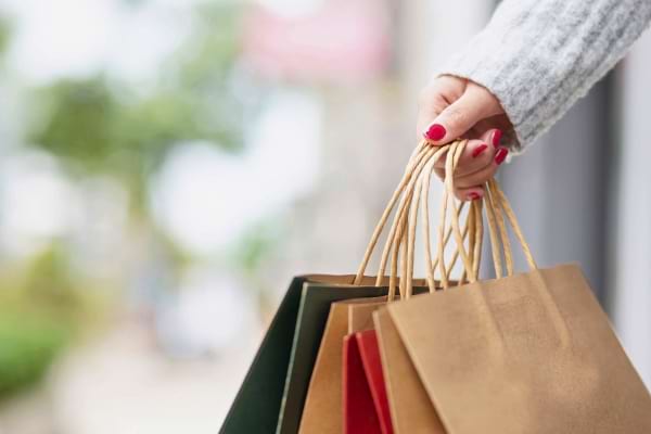 Une main porte plusieurs sacs de courses colorés en papier.