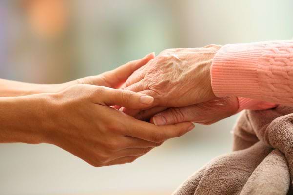 Une main jeune tient tendrement la main ridée d’une personne âgée.