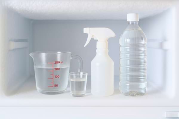 Un vaporisateur, un verre doseur et une bouteille de vinaigre placés dans un congélateur.