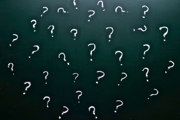 Un tableau noir est recouvert de plusieurs points d&rsquo;interrogation blancs dessin&eacute;s &agrave; la craie.