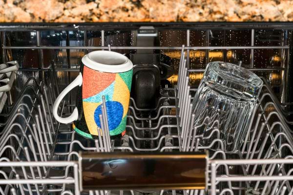 Une tasse colorée placée dans un lave-vaisselle ouvert.
