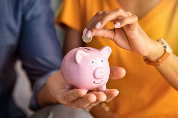 Deux personnes déposent une pièce dans une tirelire cochon rose.