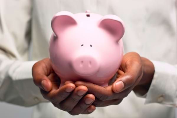 Deux mains tiennent une tirelire rose en forme de cochon.
