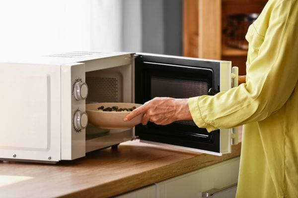 Une femme place un bol dans un micro-ondes.