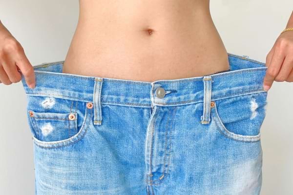 Un ventre plat apparaît avec un jean devenu trop grand, montrant une perte de poids évidente.