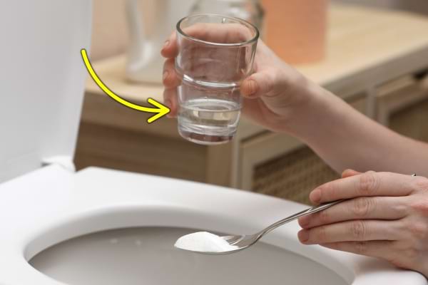 Main tenant un verre d’eau et une cuillère de bicarbonate au-dessus des toilettes.