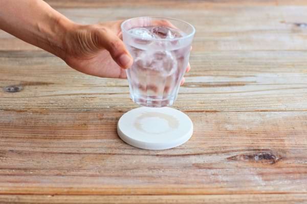 Une main pose un verre d’eau glacée laissant une trace ronde sur une table en bois.