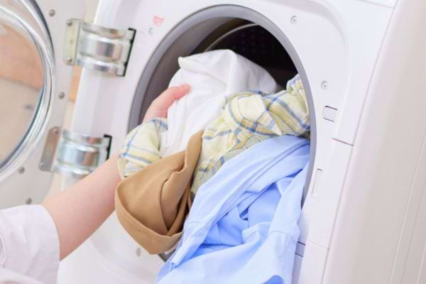 Une personne met un mélange de vêtements colorés dans une machine à laver.