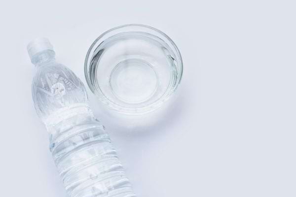 Un bol transparent et une bouteille de vinaigre blanc sont posés sur une surface claire.