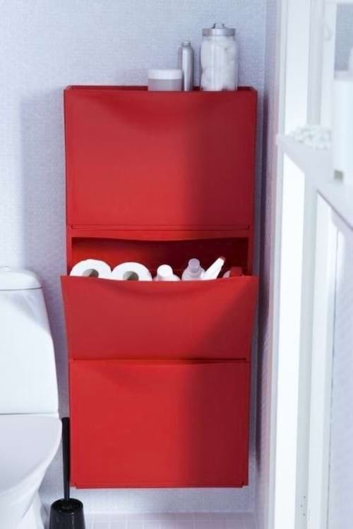 Rangement mural rouge dans une salle de bain, servant à stocker du papier toilette et d'autres accessoires.