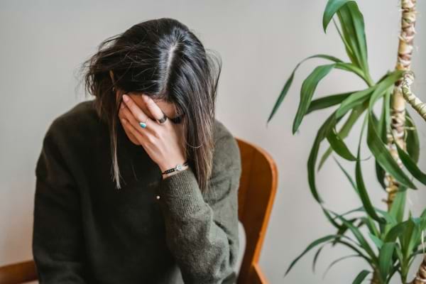 Une femme assise cache son visage avec la main, semblant fatiguée ou bouleversée.