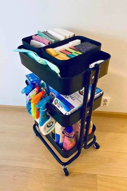 Un chariot de rangement bleu à trois étages, rempli de produits ménagers dans une buanderie.