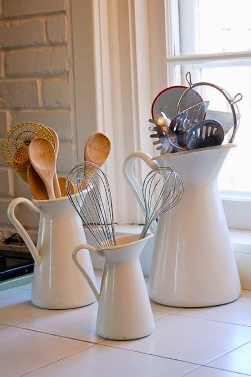 Des ustensiles de cuisine rangés dans de grands pichets en céramique blanche sur un plan de travail.
