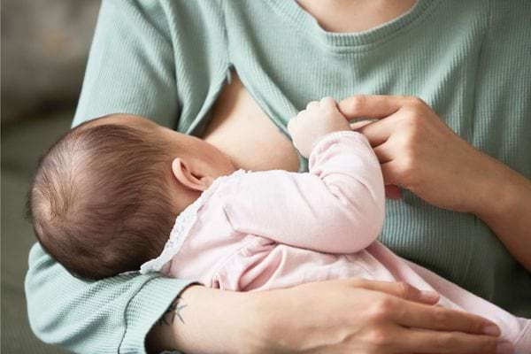 Une femme en haut vert allaite son bébé habillé en rose.
