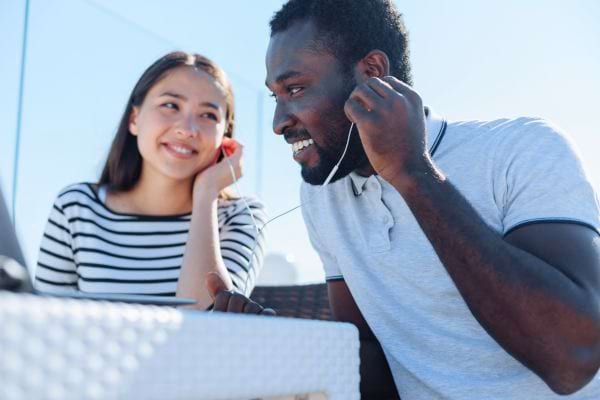 Un homme et une femme souriants partagent des écouteurs tout en écoutant de la musique à l’extérieur.