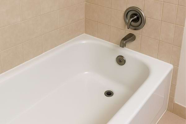 Une baignoire blanche propre installée contre un mur carrelé beige.