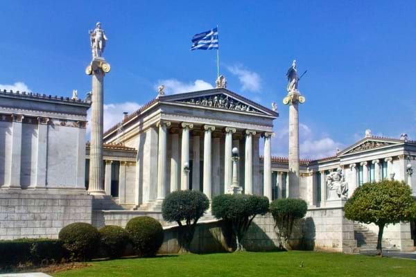 Un bâtiment grec classique avec colonnes et statues, surmonté du drapeau grec.