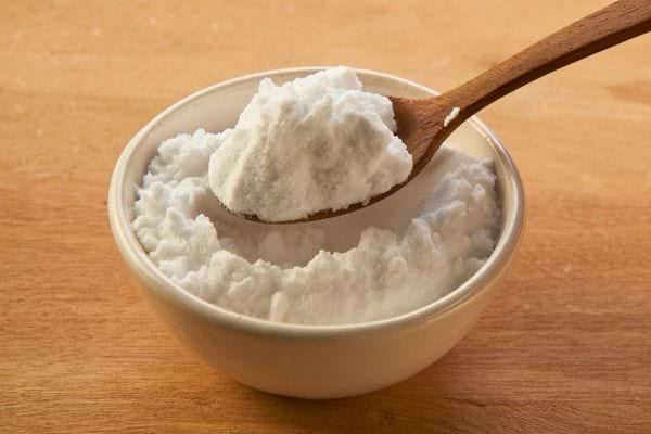 Cuillère en bois remplie de bicarbonate de soude au-dessus d’un petit bol blanc.