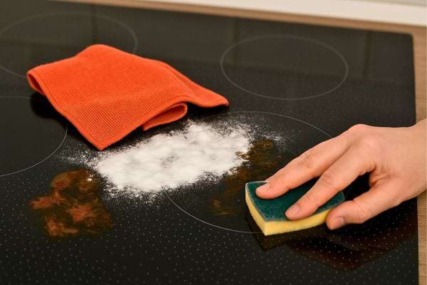 Une main frotte une plaque de cuisson avec du bicarbonate et une éponge.