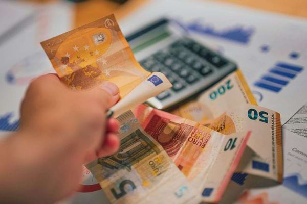 Une main compte des billets d’euros posés près d’une calculatrice sur un bureau.