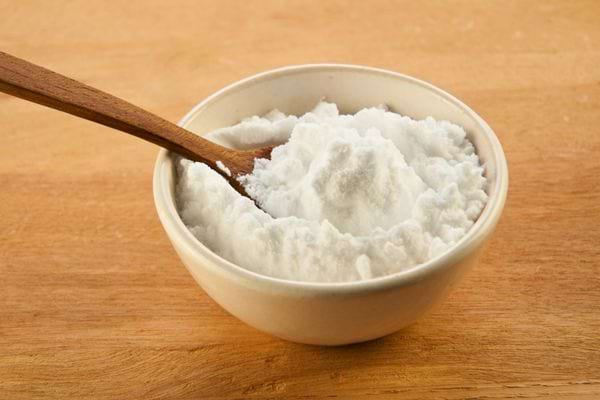 Bol blanc rempli de bicarbonate de soude avec une cuillère en bois sur fond de table.