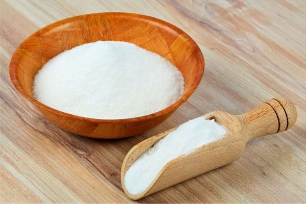 Bol en bois rempli de poudre blanche avec une cuillère doseuse assortie.