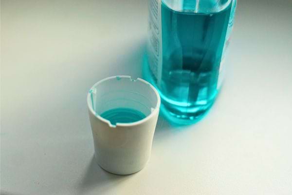 Bain de bouche bleu versé dans un bouchon doseur en plastique blanc.