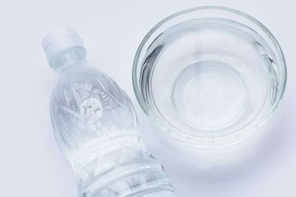 Bouteille d’eau et bol en verre transparent posés sur une surface claire pour illustrer un mélange maison.