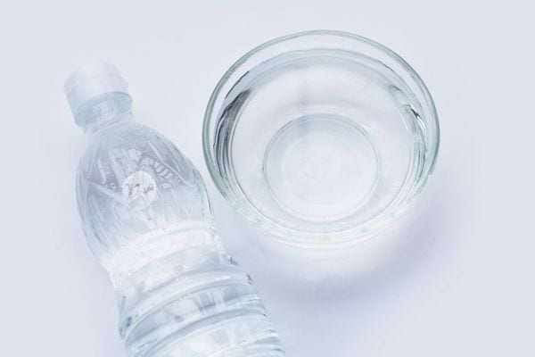 Bouteille plastique transparente et bol en verre contenant du vinaigre blanc.