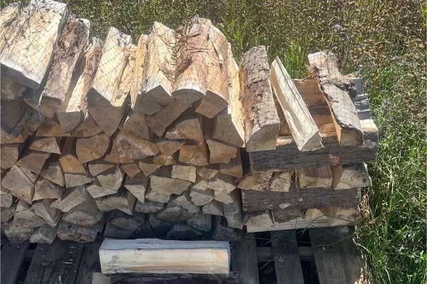 Bûches fendues soigneusement empilées sur palette à l’extérieur.