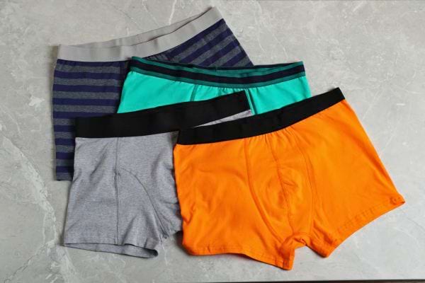 Quatre caleçons masculins de couleurs vives et variées sont soigneusement posés sur une surface grise.