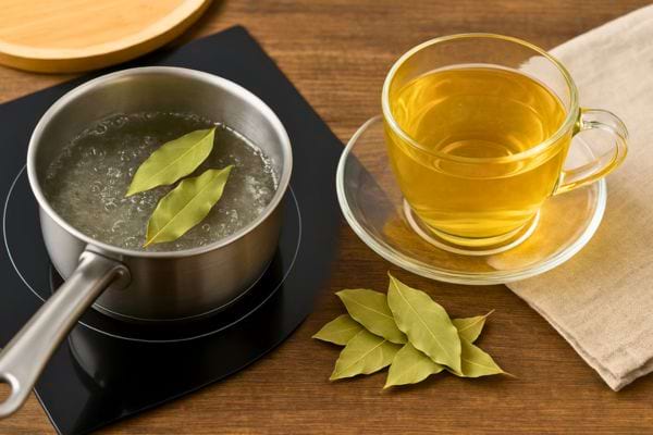 Casserole d’eau bouillante avec feuilles de laurier et tasse de tisane à côté.