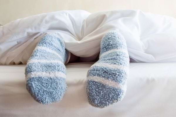Pieds couverts de chaussettes épaisses bleues et blanches sous une couette blanche.
