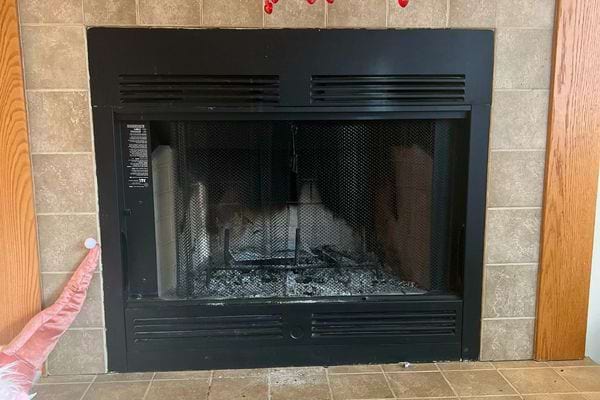 Vieille cheminée noire encastrée dans un mur carrelé avec cendres visibles.