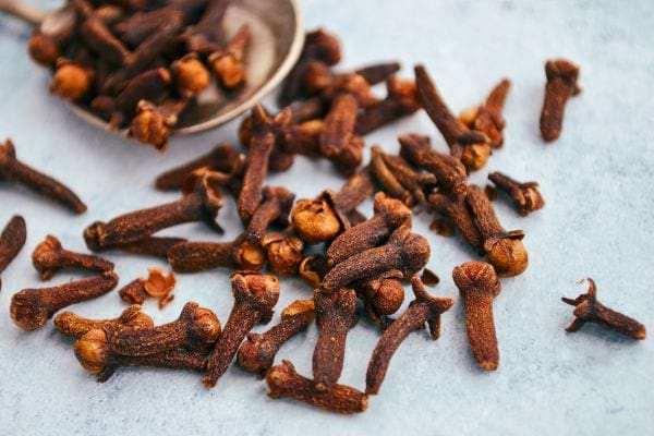 Des clous de girofle séchés sont éparpillés sur une table avec une cuillère.