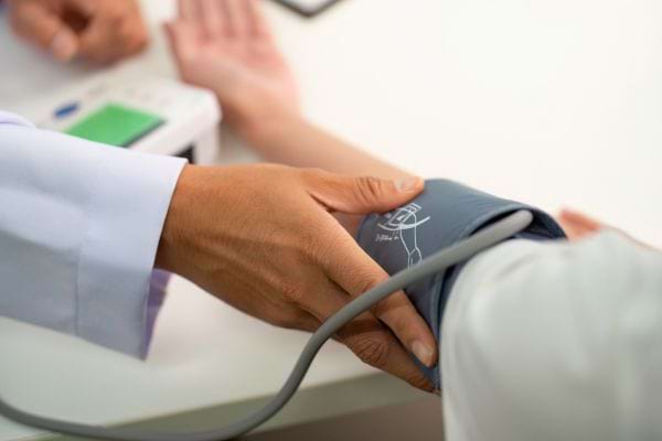 Un médecin vérifie la tension artérielle d’un patient en enroulant le brassard du tensiomètre autour de son bras.