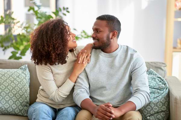 Un couple assis sur un canapé se regarde avec tendresse et complicité dans un cadre lumineux et chaleureux.