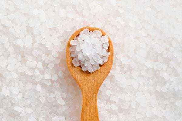 Cuillère en bois remplie de gros sel blanc sur fond de cristaux de sel.