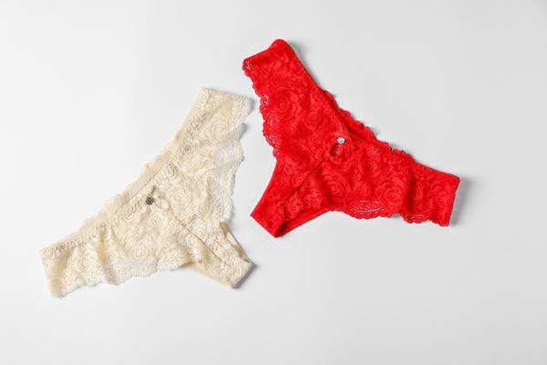 Deux culottes en dentelle, l’une rouge et l’autre beige, sont posées côte à côte sur un fond clair.