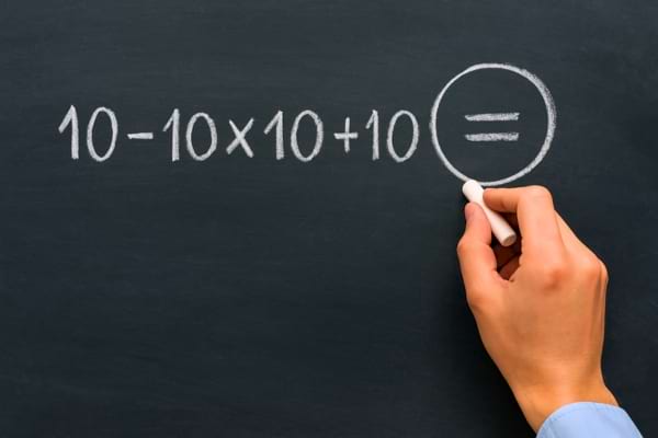 une main écrivant une équation sur un tableau noir avec un signe « = » entouré.