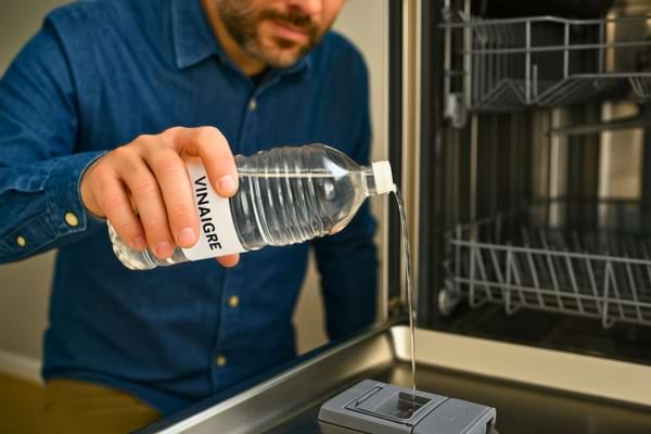 un homme qui verse du vinaigre blanc dans l'orifice du liquide de rinçage