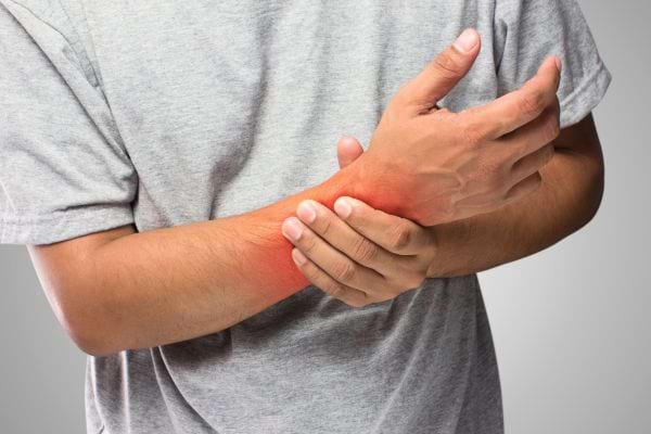 Un homme tient son poignet douloureux marqué par une inflammation rouge.