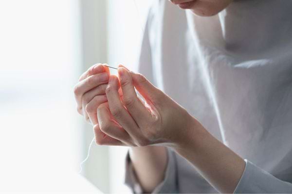Une personne enfile un fil dans une aiguille à la lumière naturelle.