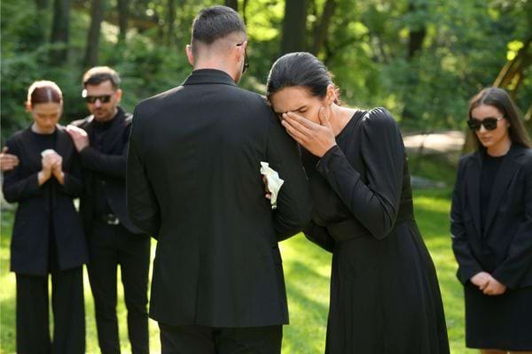 Femme en pleurs soutenue par un homme lors d’un enterrement en extérieur.