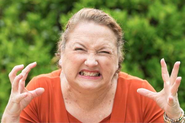 Femme d’âge mûr exprimant la colère, les dents serrées et les mains levées.