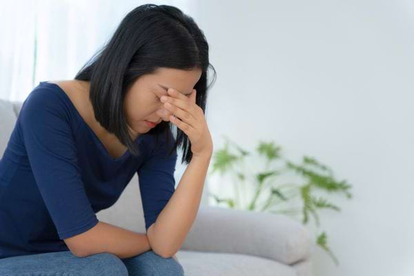 Une femme assise sur un canapé se couvre le visage de la main, accablée.